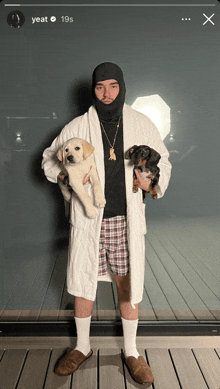 a man in a bathrobe is holding two dogs and the time is 19 s