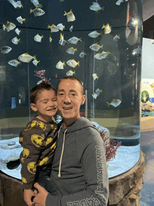 a man wearing an american eagle sweatshirt holds a child in front of a fish tank