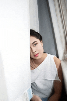 a woman sitting on a window sill with her face behind a white wall