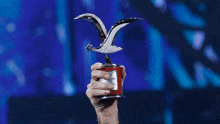 a hand is holding a trophy with a seagull on top of it