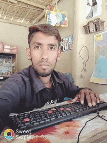 a man sitting at a desk with a keyboard and a sweet selfie app on his phone