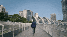 a man in a blue jacket walks across a bridge in front of tall buildings
