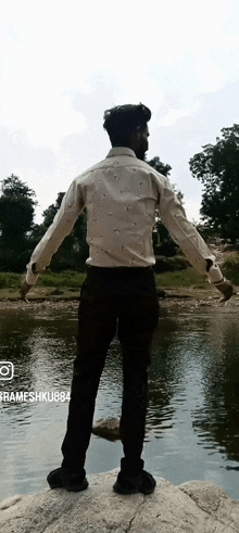 a man in a white shirt stands on a rock near a body of water with his arms outstretched