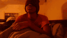 a young man wearing a red shirt and a beanie is laying on a bed