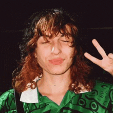 a woman with long curly hair is making a peace sign with her eyes closed .
