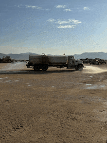 a truck is spraying something in a dirt area with mountains in the background