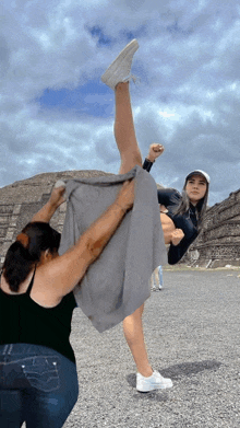 a woman in a black tank top holds a gray cloth over a woman in a white hat