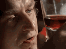 a close up of a man holding a glass of red liquid .