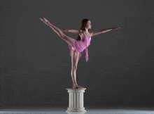 a young woman in a pink dress is balancing on a pillar