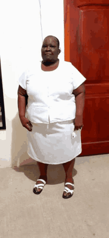 a woman in a white dress and sandals stands in front of a wooden door