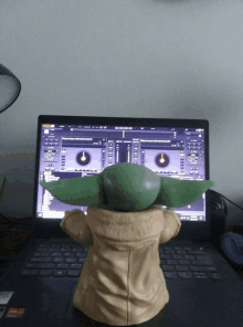 a baby yoda figurine stands in front of a laptop with a dj app open