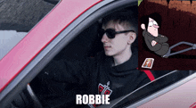 a man wearing sunglasses is sitting in a red car next to a picture of a cartoon character called robbie