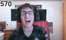 a man wearing headphones and glasses is sitting in a chair and laughing .