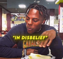a man wearing a cavaliers sweatshirt sits at a table with a burrito