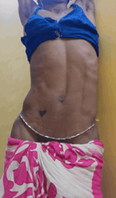 a woman in a blue top and pink and white skirt has a heart tattoo on her belly