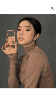 a woman in a brown turtleneck is holding a palette with a diamond on it