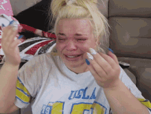 a woman wearing a ucla shirt is crying with her eyes closed