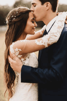 a bride and groom kissing in a field with the bride wearing a flower crown