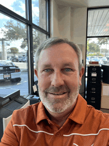 a man with a beard wears an orange shirt with the letter t on the front