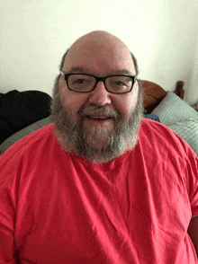 a bald man with glasses and a beard wears a red shirt