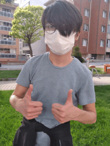 a young man wearing a face mask and glasses giving a thumbs up