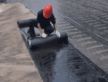 a man wearing a hard hat is rolling a roll of bitumen on a roof .