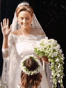 a woman in a wedding dress holds a bouquet of white flowers while a little girl wearing a flower crown looks on