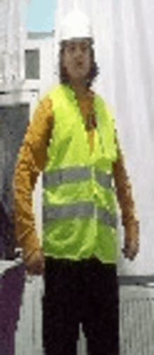 a man wearing a yellow vest and a white hard hat is standing in front of a window .