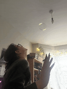 a woman reaches up to catch a soap bubble hanging from the ceiling