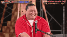 a man in a red jacket is smiling in front of a microphone with chinese writing on it .