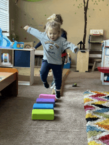 a little girl wearing a shirt that says bobcats is jumping over blocks