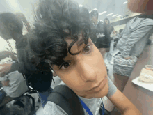 a young man with curly hair takes a selfie in a cafeteria