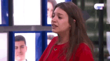 a woman in a red shirt is crying while standing in front of a wall of pictures .