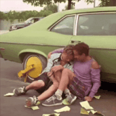 two men are sitting next to a green car with a yellow wheel lock
