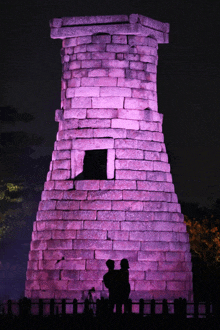 a couple standing in front of a brick tower lit up in purple