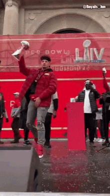 a man in a red jacket is holding a trophy in front of a banner that says super bowl liv