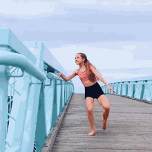 a young girl in a pink top and black shorts is standing on a wooden bridge with one leg up