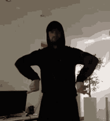 a man in a black hoodie stands with his hands on his hips in a living room