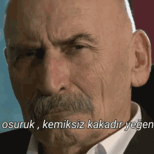 a bald man with a mustache is making a funny face with the words " osuruk kemiksiz kakadir yegen " below him