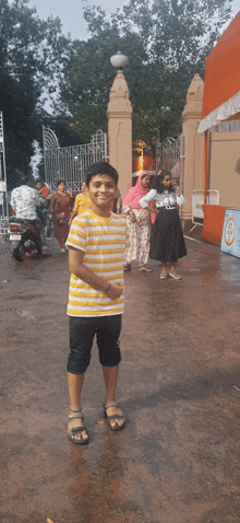 a boy wearing a yellow and black striped shirt stands in front of a building