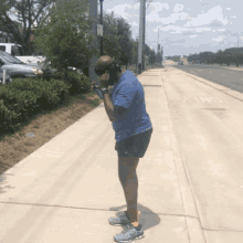 a man wearing a blue shirt and black shorts stands on a sidewalk with the word only written on it