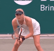 a woman is holding a tennis racquet on a tennis court in front of a green sign that says brin