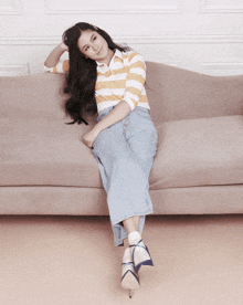 a woman sitting on a couch wearing a striped shirt and jeans