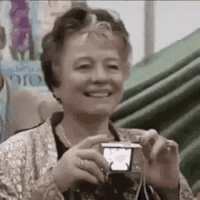 an elderly woman is smiling while holding a small camera .