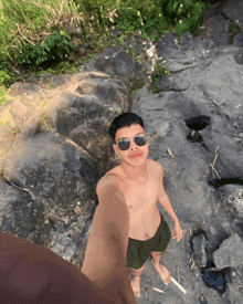 a shirtless man wearing sunglasses is standing on a rock