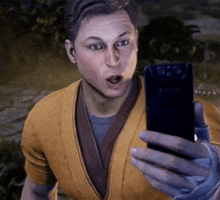 a man in a yellow shirt is holding a cell phone and looking at it