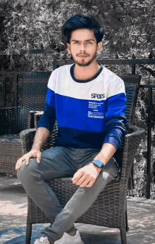 a young man is sitting in a chair wearing a blue and white shirt that says spots