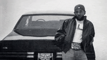 a man with a beard is standing in front of a black car .