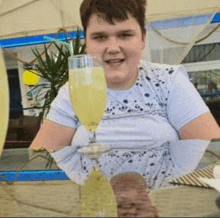 a young man is sitting at a table holding a glass of liquid .