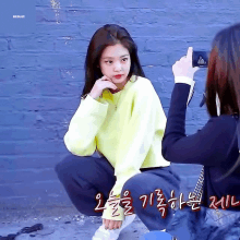 a girl in a yellow sweater is squatting down while another girl takes a picture